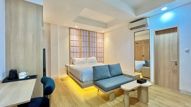 A modern hotel room with a bed, a desk, a chair, a small table, and a wardrobe. - Jambuluwuk Mansion Adityawarman (Jakarta)