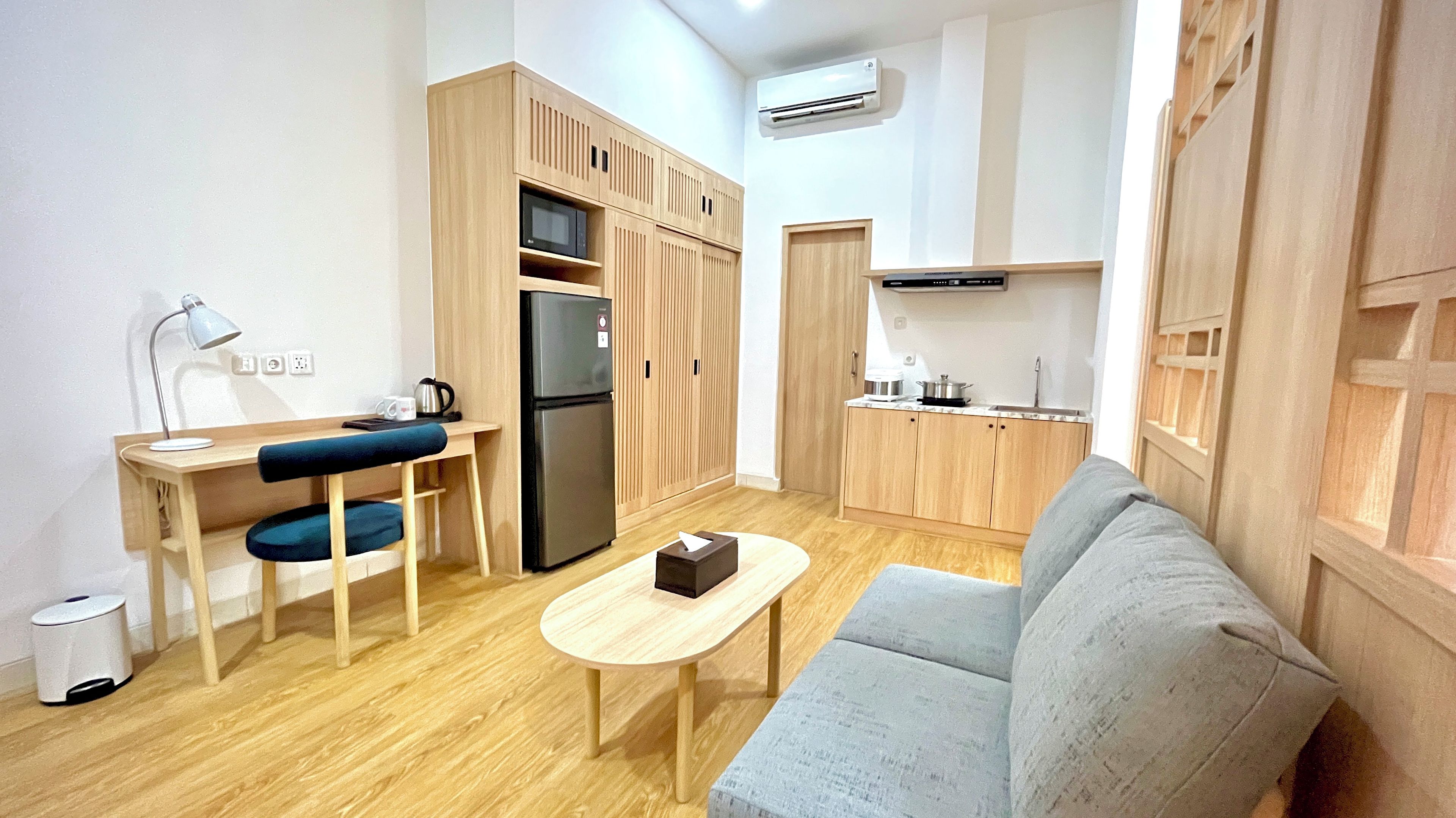 Un espacio habitable compacto con kitchenette, un sofá, una mesita y un escritorio con silla.