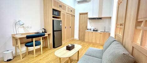 A compact living space with a kitchenette, a sofa, a small table, and a desk with a chair.