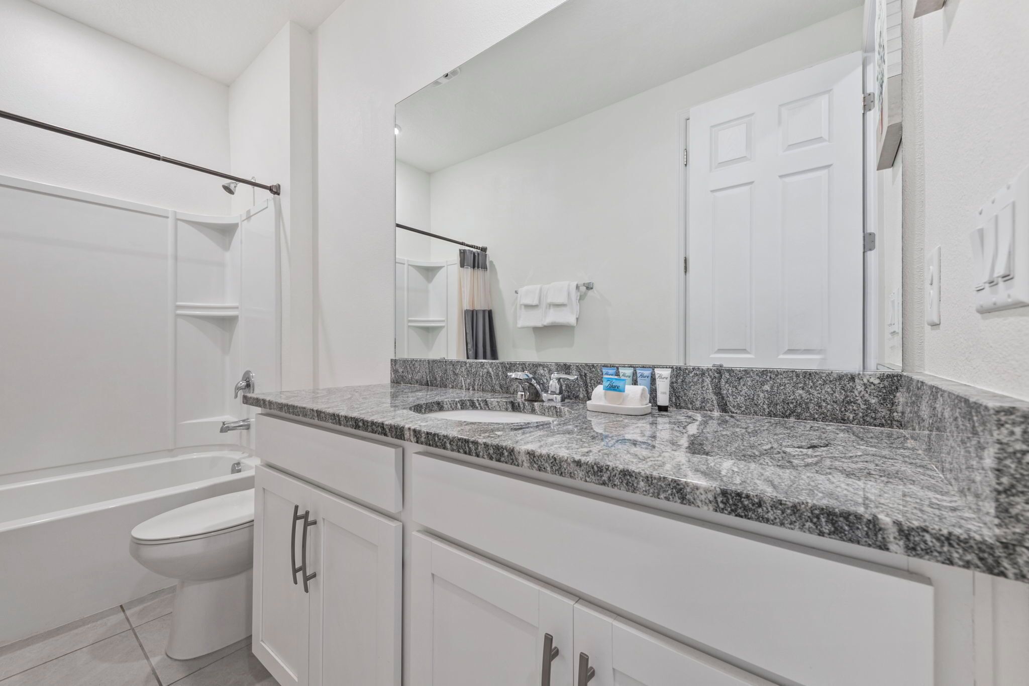 A modern bathroom with a white toilet, a granite countertop sink, and a large mirror.