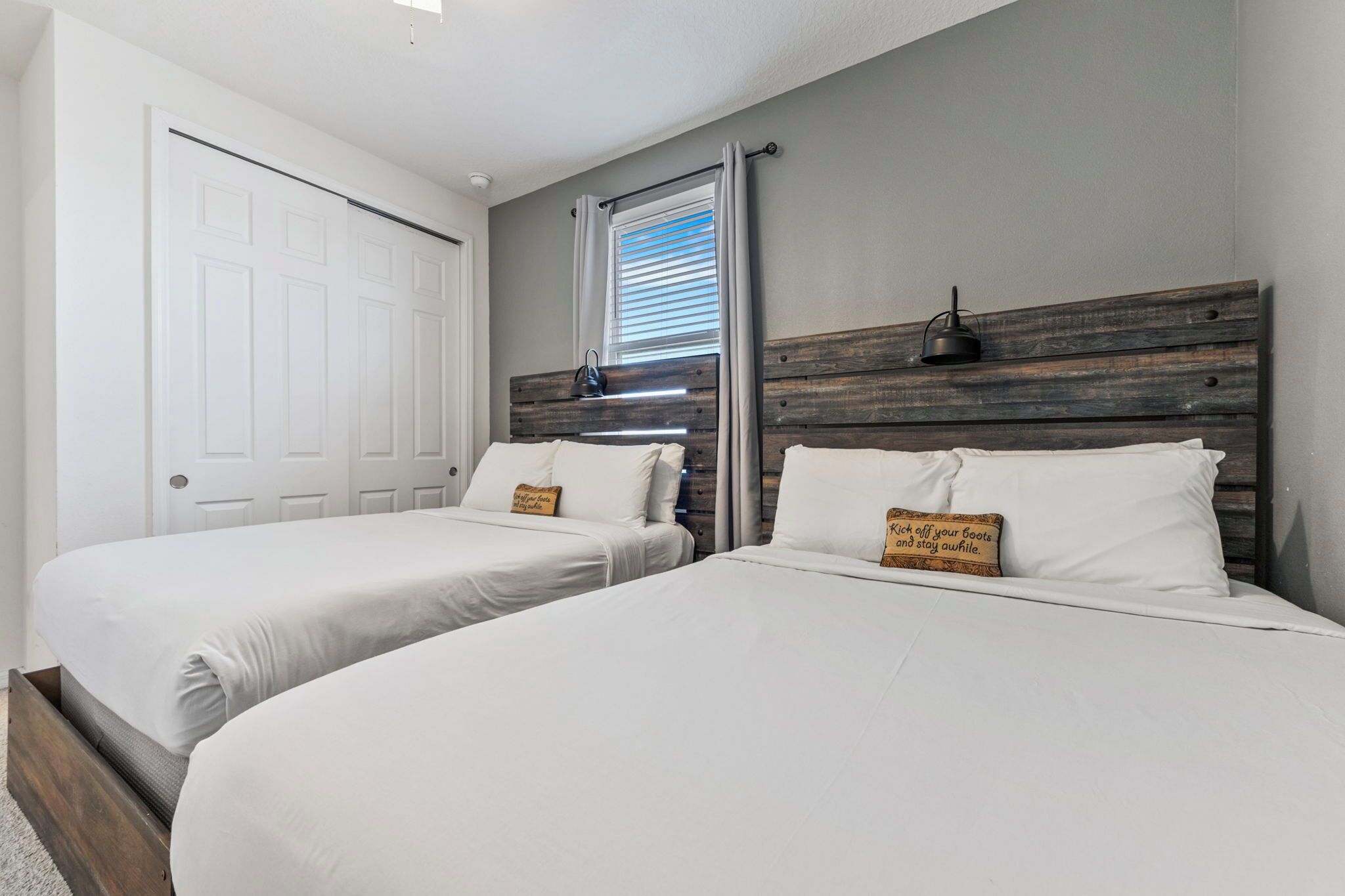 Une chambre avec deux lits, une tête de lit en bois, une fenêtre avec des stores et une porte blanche.