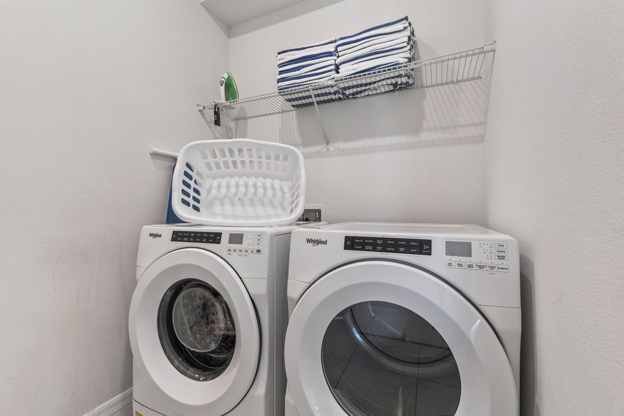 Deux machines à laver Whirlpool à chargement frontal se trouvent dans une buanderie, avec un panier blanc posé sur le dessus.