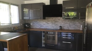 A modern kitchen with dark cabinetry, a tiled backsplash, and stainless steel appliances. - AIR-CONDITIONED VILLA WITH POOL AND SPA - GOLFE DE SAINT-TROPEZ (Le Plan-de-la-Tour)