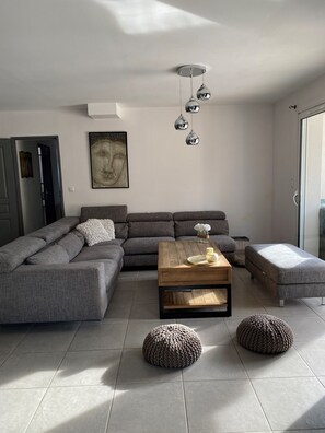 Ein modernes Wohnzimmer mit einem Ecksofa, einem Holztisch und zwei Poufs.