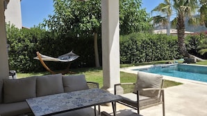 An outdoor patio with a sofa, chairs, a table, a hanging light, and a pool. - AIR-CONDITIONED VILLA WITH POOL AND SPA - GOLFE DE SAINT-TROPEZ (Le Plan-de-la-Tour)