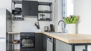 Una cocina moderna con horno empotrado, lavavajillas y cafetera. Cuenta con una encimera de madera y un mueble negro sobre el fregadero.