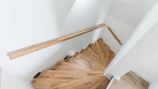Una escalera de madera con barandilla y un pasamanos de madera en la pared.