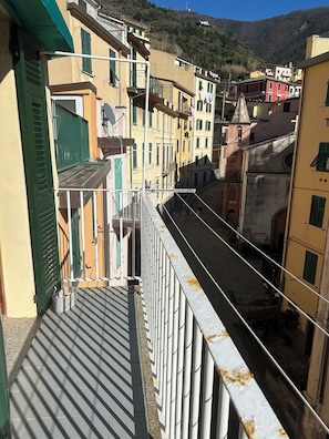 Uma rua estreita com edifícios em ambos os lados, varandas com grades e vista clara da colina circundante.