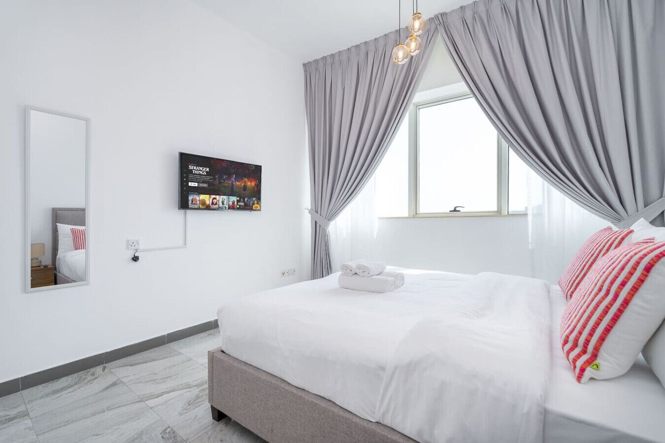 Une chambre d’hôtel moderne avec un grand lit, des rideaux gris, un téléviseur fixé au mur et une fenêtre donnant sur un beau paysage.