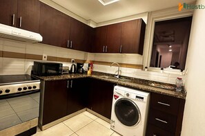 Cocina compacta con armarios de madera oscura, microondas integrado, estufa y lavadora de carga frontal.