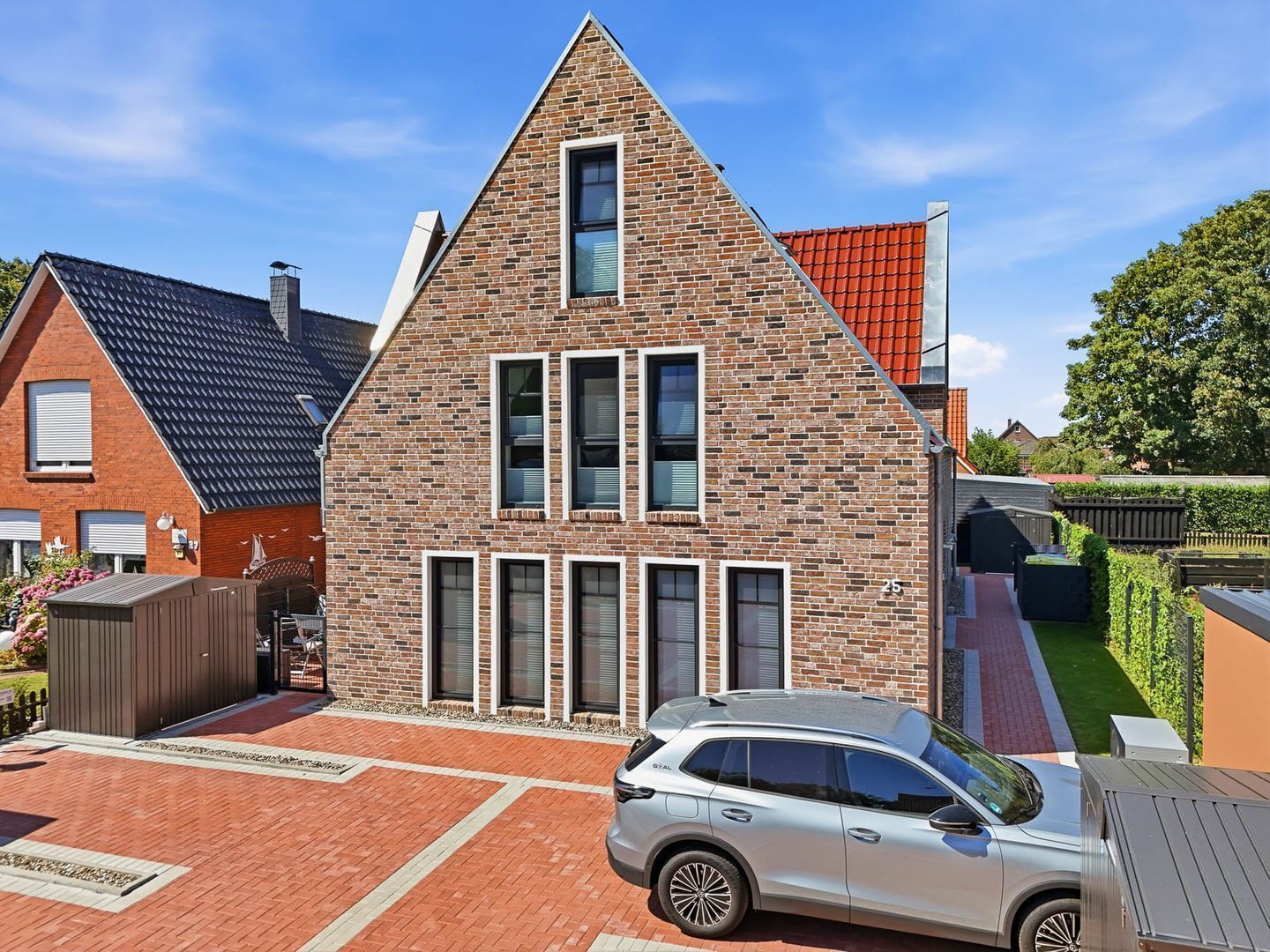 A modern two-story house with a brick facade, multiple windows, and a car parked in the driveway.