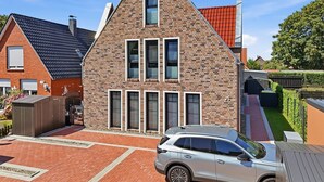 Une maison moderne à deux étages, avec une façade en briques, de nombreuses fenêtres et une voiture garée dans l’allée.