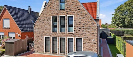A modern two-story house with a brick facade, multiple windows, and a car parked in the driveway.