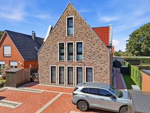 A modern two-story house with a brick facade, multiple windows, and a car parked in the driveway. - Cordula - Modern vacation apartment Cordula with garden, terrace and e-charging station (Krummhörn)