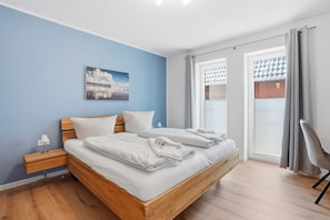 A bedroom with a bed, a nightstand, a lamp, a window with curtains, and a chair. - Cordula - Modern vacation apartment Cordula with garden, terrace and e-charging station (Krummhörn)