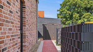 Une étroite allée pavée de briques rouges, avec une clôture en métal et un bâtiment gris dont la porte porte l’inscription « Cordula ».