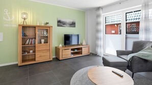 Un salon comprenant un téléviseur, une bibliothèque, un canapé gris et une table basse ronde.