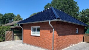 A brick building with a blue roof, a window, and a door. - Haus Seestern - Holiday home Seestern with modern furnishings and fenced garden (Cuxhaven)
