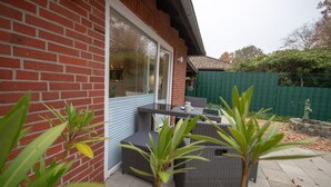 A patio with wicker furniture, a brick wall, and a green fence. - Haus Seestern - Holiday home Seestern with modern furnishings and fenced garden (Cuxhaven)