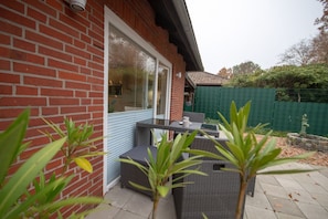 A patio with wicker furniture, a brick wall, and a green fence. - Haus Seestern - Holiday home Seestern with modern furnishings and fenced garden (Cuxhaven)