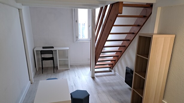 A room with a white desk, black chair, and a black ottoman. There is a wooden staircase leading to an upper level. - Mezzanine studio full (Bordeaux)