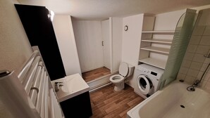 A compact bathroom with a toilet, washing machine, and bathtub. - Mezzanine studio full (Bordeaux)