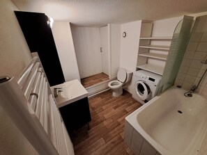A compact bathroom with a toilet, washing machine, and bathtub. - Mezzanine studio full (Bordeaux)