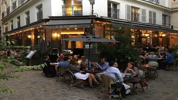Een terras met tafels en stoelen, omringd door gebouwen.