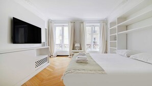 Een hotelkamer met een groot bed, een aan de muur bevestigde televisie en een balkon met gordijnen.