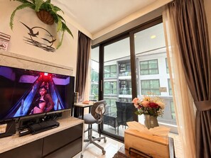 A hotel room with a television, a desk, a chair, a vase with flowers, and a large window with curtains. - A101 - 1 Bedroom Serviced Apartment at Ao Nang Beach (Tambon Ao Nang)