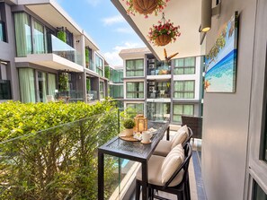 Ein Balkon mit Tisch, Stühlen, hängenden Blumenkörben und einem Gemälde mit Strandmotiv.