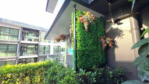 Ein modernes Gebäude mit Balkon, einer grünen Wand mit hängenden Blumenkörben und einem Vogelhaus.