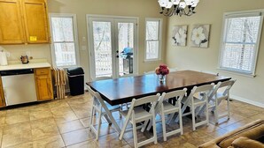 Una cocina con una mesa de comedor, sillas, una araña y vistas a través de puertas de vidrio.