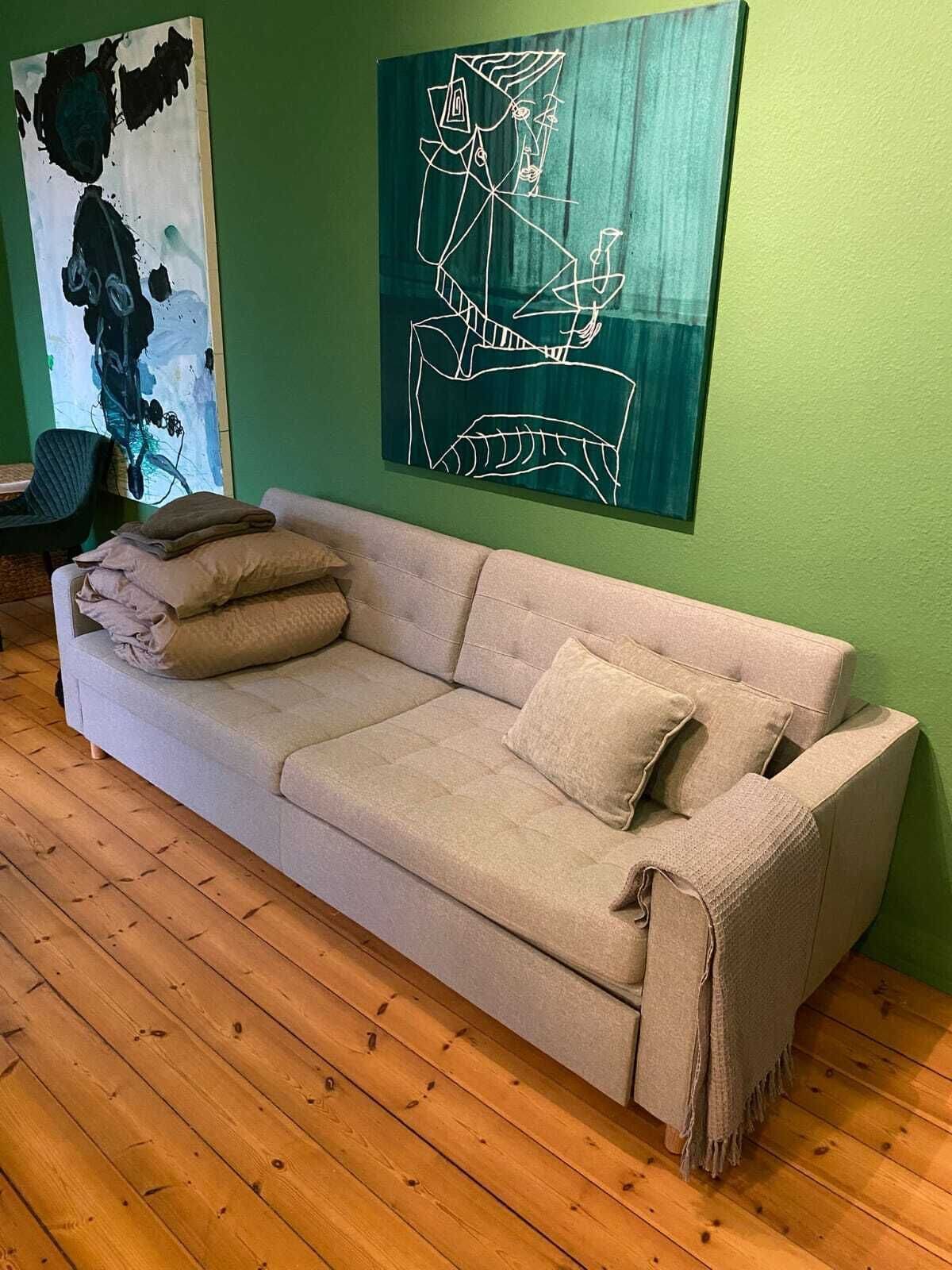 A beige sofa with pillows and a blanket, a green wall, and a painting.