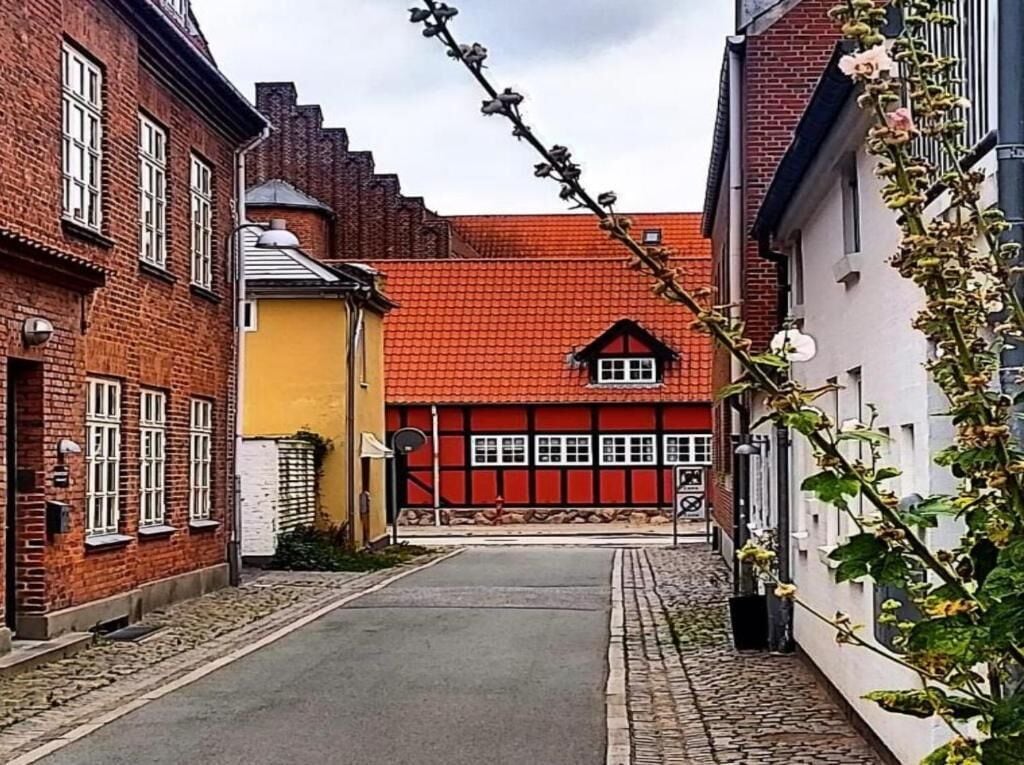 A narrow street with traditional buildings, one with a red-tiled roof and another with a yellow facade.