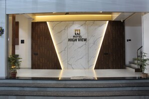 Zona de recepción de hotel con pared de mármol, puertas de madera y una escalera que conduce a los pisos superiores.