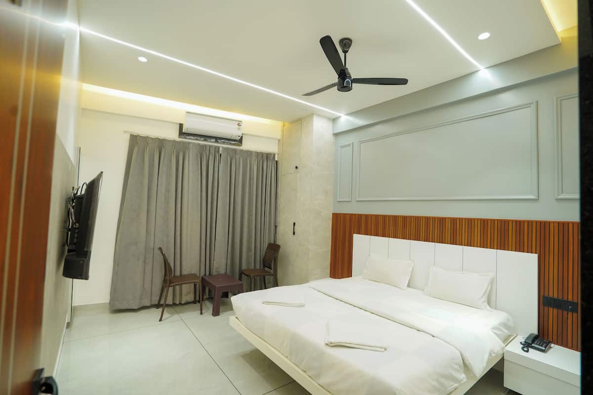 A hotel room with a bed, a ceiling fan, a TV, a chair, a small table, and an air conditioning unit.
