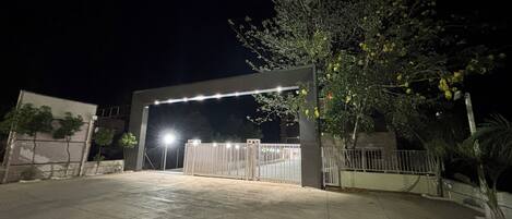 Une entrée fermée par un portail et une clôture en métal, un arbre aux fleurs jaunes et un bâtiment en arrière-plan.