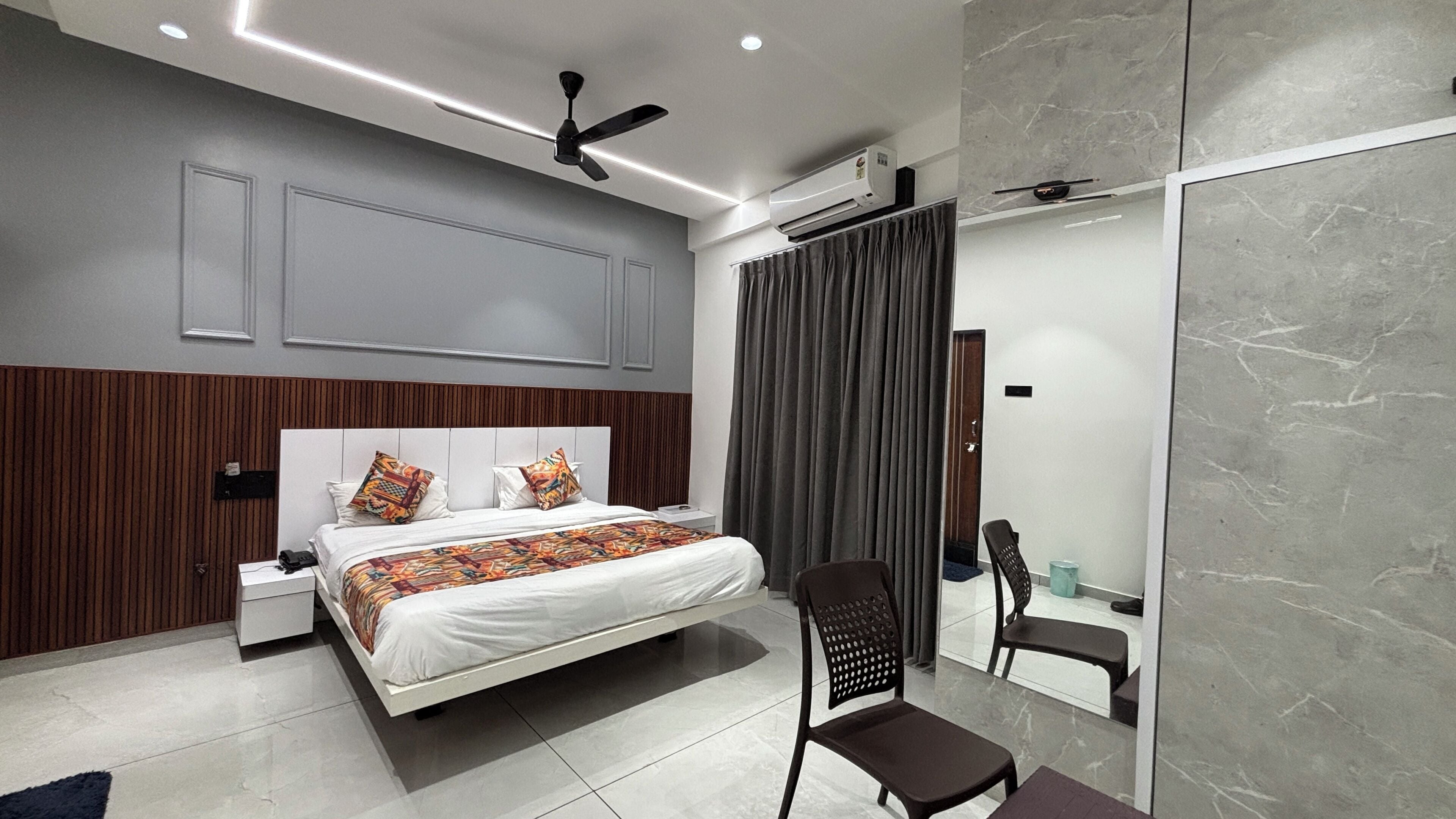 A modern bedroom with a bed, bedside tables, a chair, a ceiling fan, and a large mirror.