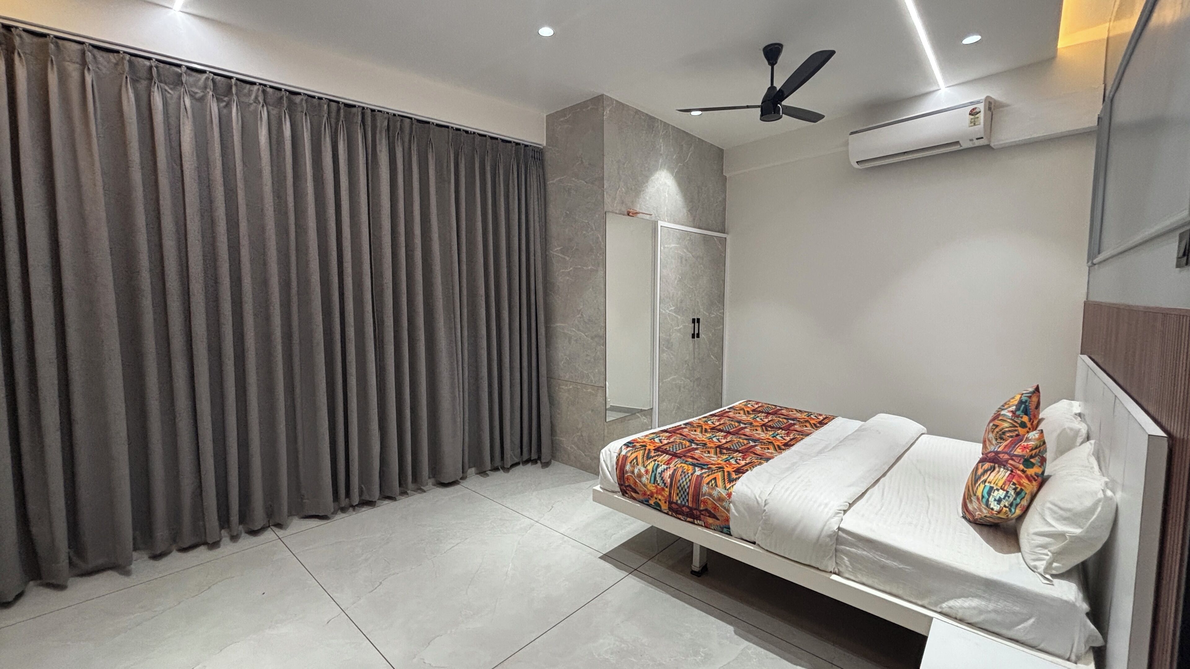 A modern bedroom with a bed, curtains, a ceiling fan, and an air conditioning unit.