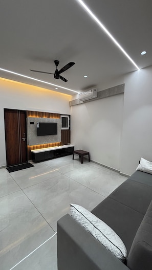 A modern living room with a flat-screen TV, ceiling fan, and built-in air conditioning unit.