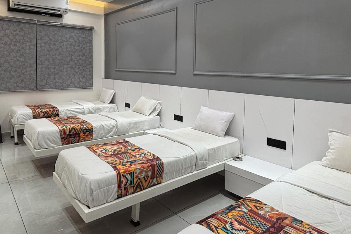 A modern hotel room with three beds, a ceiling fan, recessed lighting, and a large window with blinds.