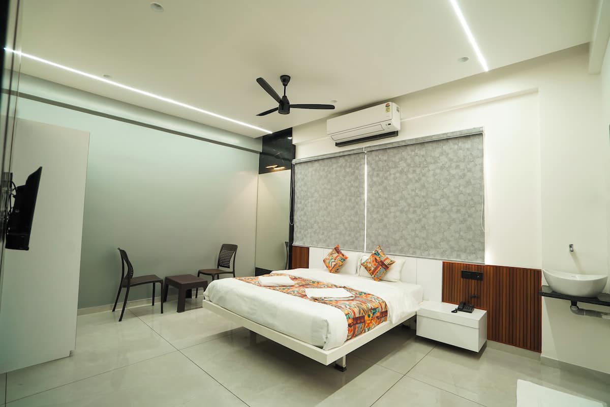 A modern hotel room with a bed, bedside table, chair, and a large window with a patterned curtain.