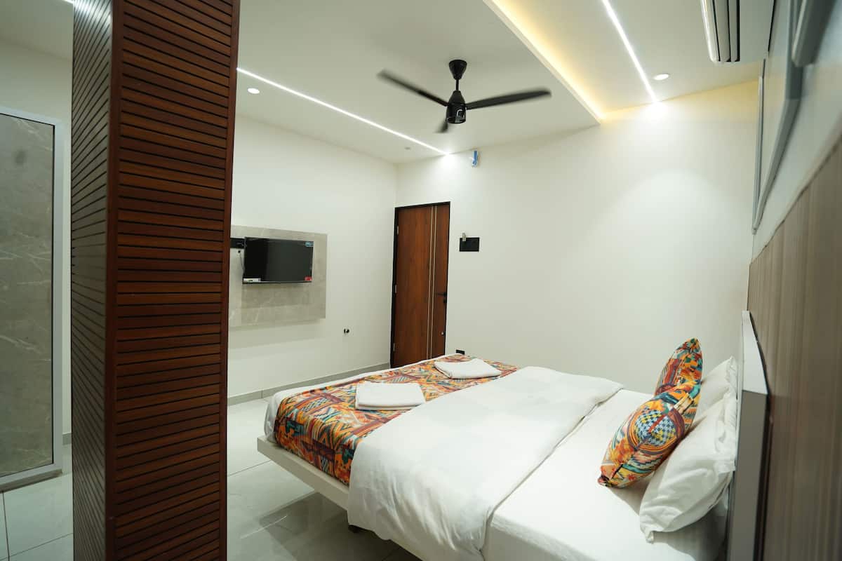 A modern hotel room with a bed, a ceiling fan, a TV mounted on the wall, and a wooden panel on one side.