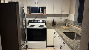 Une cuisine de taille réduite équipée d’un réfrigérateur, d’un four à micro-ondes, d’une cuisinière et d’un plan de travail en granit.