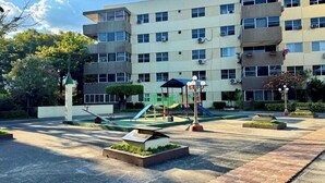 Un immeuble à plusieurs étages, avec un espace de jeux situé devant, comprenant des toboggans et des balançoires.
