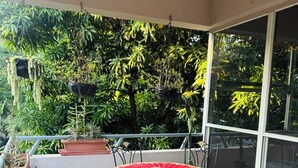 Un balcon avec une table ronde et des chaises, entouré de plantes en pot et offrant une vue sur un feuillage dense.