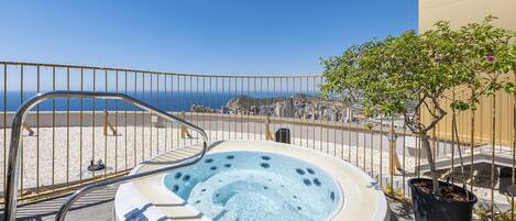 A hot tub on a deck with a view of the sea and a building in the background.