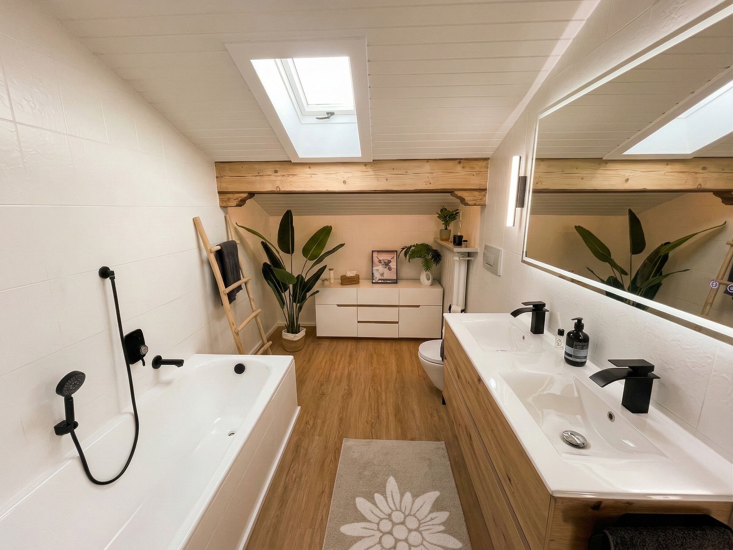 Une salle de bain moderne avec un puits de lumière, deux lavabos, une baignoire et un revêtement de sol en bois.