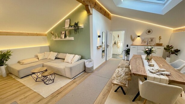 Een moderne woonkamer met een bank, een eettafel en stoelen. Boven de eethoek bevindt zich een dakraam.